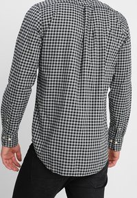 Koszula w czarno-białą kratę, z długimi rękawami, slim-fit design, z wydłużonym kołnierzykiem i zapięciem na guziki przy mankietach. Tył koszuli ma detal w postaci zaszewki.