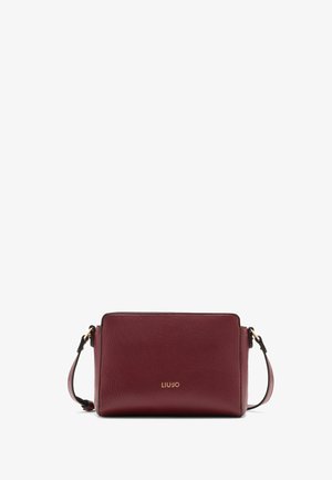 Burgundy leather crossbody bag with a textured finish, gold logo on the front, and an adjustable strap. Rectangular shape and minimalistic design.