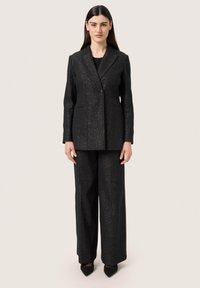 Fekete, szabott öltöny texturált felülettel, egy gombos záródással, kivágott hajtókával és széles lábú nadrággal.