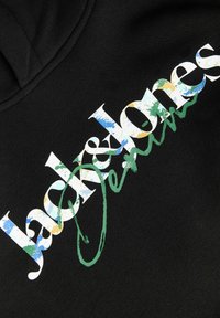 Tissu noir avec le texte multicolore « Jack & Jones » et le mot « Jeans » en vert cursif écrit en diagonale sur le tissu.