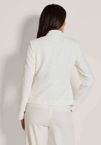 Witte gestructureerde blazer met lange mouwen, met subtiele glansaccenten en een getailleerd ontwerp. De achterkant heeft een hoge kraag en een op maat gemaakte pasvorm.