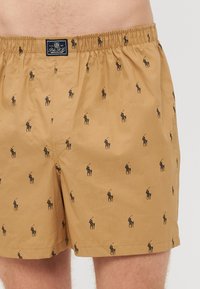 Barna boxer alsónadrág, rugalmas derékpánttal, amelyen fekete póni logó minta ismétlődik, könnyű anyagból készült.