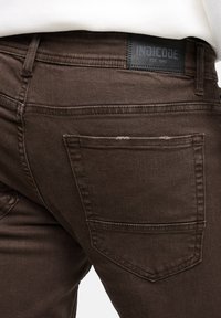 Brązowe dżinsy Denim o dopasowanym kroju, z teksturowaną powierzchnią i tylną kieszeń z widocznym szwem. Metka marki na talii.