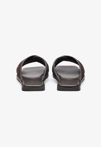 Brune lær slip-on sandaler med flad sål, der har et tekstureret stropdesign og åben tå, set fra bagfra.