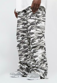 Kárované cargo kalhoty v šedé a bílé barvě, volného střihu, s několika kapsami a nášivkou na stehně. Vyrobené z lehkého materiálu.