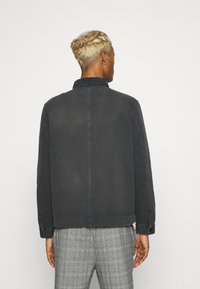 Sort denimjakke med knapkrave, sidelommer og løs pasform. Tekstureret stof med en let falmet overflade.