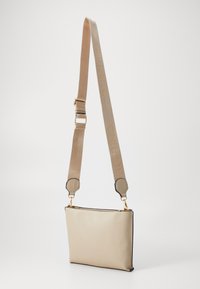 Borsa a tracolla in pelle beige con una texture liscia, forma rettangolare e hardware tono oro. La tracolla regolabile presenta un marchio inciso.