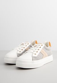 Sneaker bianche con una punta in pelle liscia, pannelli in feltro grigio, dettagli beige, occhielli dorati e una suola in gomma testurizzata.
