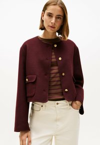 Bordeaux cropped jack gemaakt van gestructureerde stof, met gouden knopen, een ronde halslijn en twee voorzakken. Gedragen over een gestreepte top.