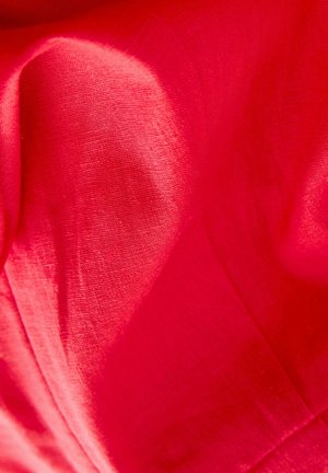 Tessuto rosso brillante con una superficie liscia, che mostra lievi pieghe e drappeggi morbidi. Il materiale appare leggero e traspirante.