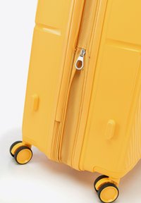 Valigia rigida gialla con superficie texturizzata, doppia cerniera e due ruote nere con bordi gialli per una facile mobilità.