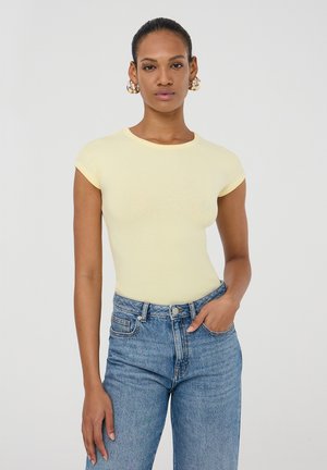 T-shirt giallo a maniche corte, aderente, con scollatura rotonda, abbinato a jeans in denim blu a vita alta, con design classico a cinque tasche.