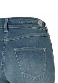 Vue arrière d'un jean en denim bleu montrant une seule poche arrière, une boucle de ceinture et du texte de marque brodé décoloré sur la taille.