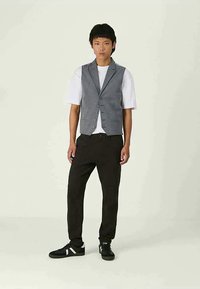 Vestă gri cu model purtată peste o cămașă albă, combinată cu pantaloni negri și adidași negri. Vesta are închidere cu nasturi și croială ajustată.