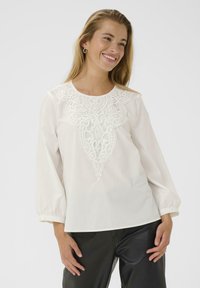 Weißes Bluse mit gestickten Details auf der Vorderseite, Rundhalsausschnitt und langen Ärmeln. Kombiniert mit schwarzen Hosen. Glatt, leichtes Material.