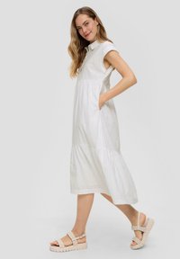 Witte, knielange jurk gemaakt van lichtgewicht stof met een kraag, korte mouwen en broderie anglaise details. In combinatie met beige sandalen.