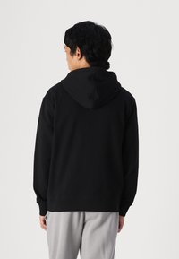 Sudadera negra con capucha, hecha de algodón, que presenta un corte relajado, puños y dobladillo acanalados. La parte posterior muestra una textura suave sin logos visibles.