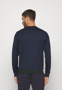 Camisa de manga larga azul marino hecha de un tejido suave, con un dobladillo acanalado verde en la parte inferior y un clásico escote redondo.