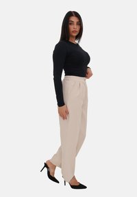 Top nero a maniche lunghe abbinato a pantaloni beige su misura con chiusura a bottone, indossato con scarpe con tacco nere. Design semplice.