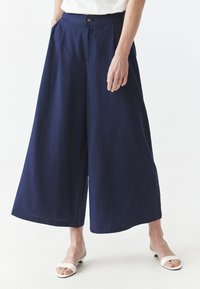 Pantalones de pierna ancha en color azul marino con cintura alta, pliegues, bolsillos frontales y cierre de botón, confeccionados en una tela suave y ligera.
