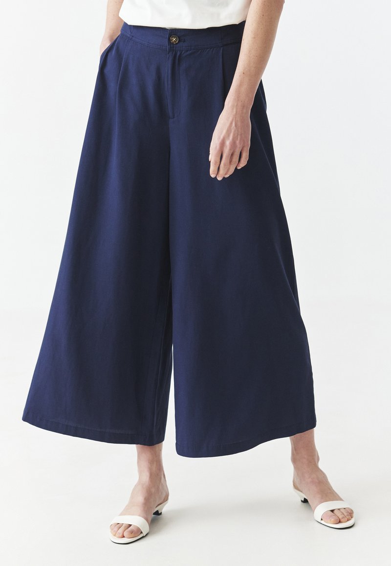 Pantalones de pierna ancha en color azul marino con cintura alta, pliegues, bolsillos frontales y cierre de botón, confeccionados en una tela suave y ligera.