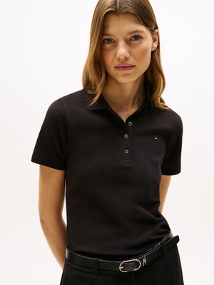 Svart polo-skjorte med korte ermer, med en tre-knapps knapping og liten logo. Brukt med et svart belte og bukser med høy liv.