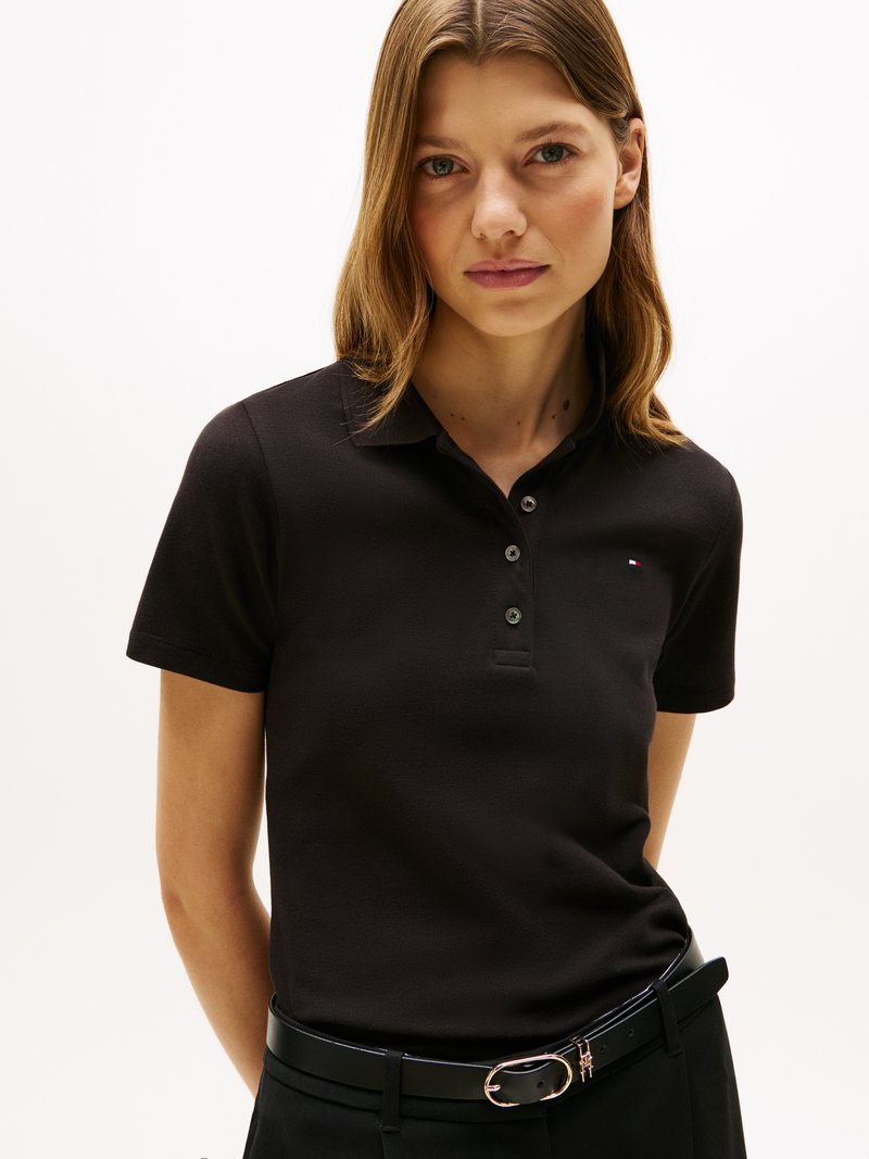 Chemise polo noire à manches courtes, avec une patte de boutonnage à trois boutons et un petit logo. Associée à une ceinture noire et un pantalon taille haute.