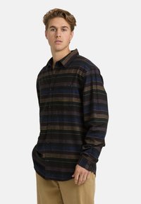 Zwart-blauw geruit flanellen overhemd met blauwe, bruine en bordeauxrode strepen; knoopsluiting aan de voorkant, lange mouwen en één borstzak.