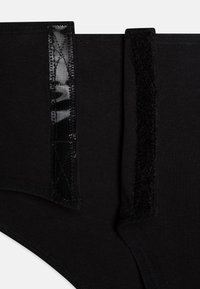 Culotte taille haute noire avec un tissu texturé, des accents brillants et en velours sur les côtés, des bords cousus et une finition lisse.