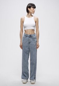 Balts īsais topiņš ar pelēkām platām džinsa biksēm, kas ir ar augstu vidukli, priekšējām kabatām un sānu šķēlumiem pie apakšmalas. Balti sporta apavi.