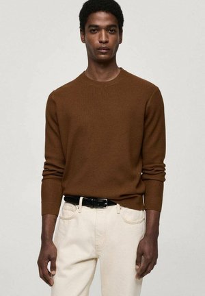 Brown ribbed knit sweater with long sleeves, crew neckline, worn with light-colored jeans and a black belt. Plain background.