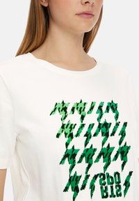 Weißes Baumwoll-T-Shirt mit grünem geometrischen Muster in unterschiedlichen Farbtönen und Texturen. Rundhalsausschnitt, normale Passform.