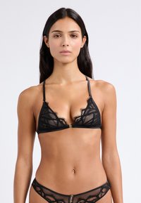 Soutien-gorge en dentelle noire avec des bonnets triangulaires aux bords festonnés, des détails en dentelle délicate, des bretelles ajustables et un petit fermoir en or au centre.