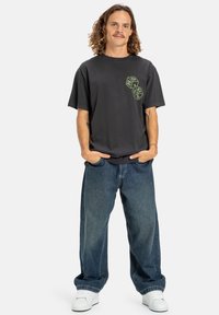Sort kortærmet t-shirt med grønt terningmotiv på brystet, parret med løse blå denimjeans og hvide sneakers.