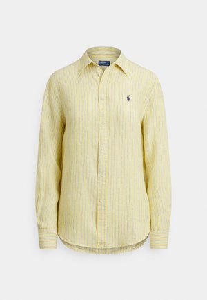 Dzeltens krekls ar garām piedurknēm un pogām, ar vertikālām baltām un zilām svītrām, mazs zils izšūts logo uz kreisās krūtīm un smails apkaklis.