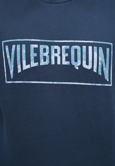 Ύφασμα σκούρου μπλε με ένα ορθογώνιο λογότυπο σε ανοιχτό μπλε και λευκό μοτίβο που αναγράφει "VILEBREQUIN" στο κέντρο του.
