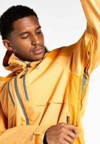 Gelbe Outdoor-Jacke mit grauen Akzenten, hoher Kragen, mehreren mit Reißverschluss versehenen Taschen und einem leichten, strukturierten Stoff.
