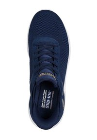 Zapatilla deportiva sin cordones de color azul marino, con parte superior de malla, plantilla acolchada y suela blanca. Presenta patrones texturizados y cordones elásticos.