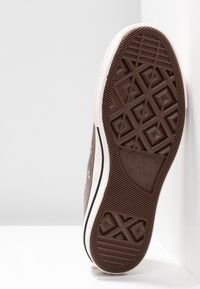 Semelle en caoutchouc marron de la basket Converse All Star montrant le motif de la semelle et la taille 43, inclinée sur un fond blanc.