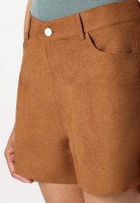 Brown faux suede shorts feature a smooth texture, standard pockets, and a button closure. The design is tailored for a fitted silhouette.