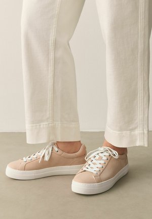 Light beige low-top sneakers with white laces and thick white soles worn with off-white straight leg pants.