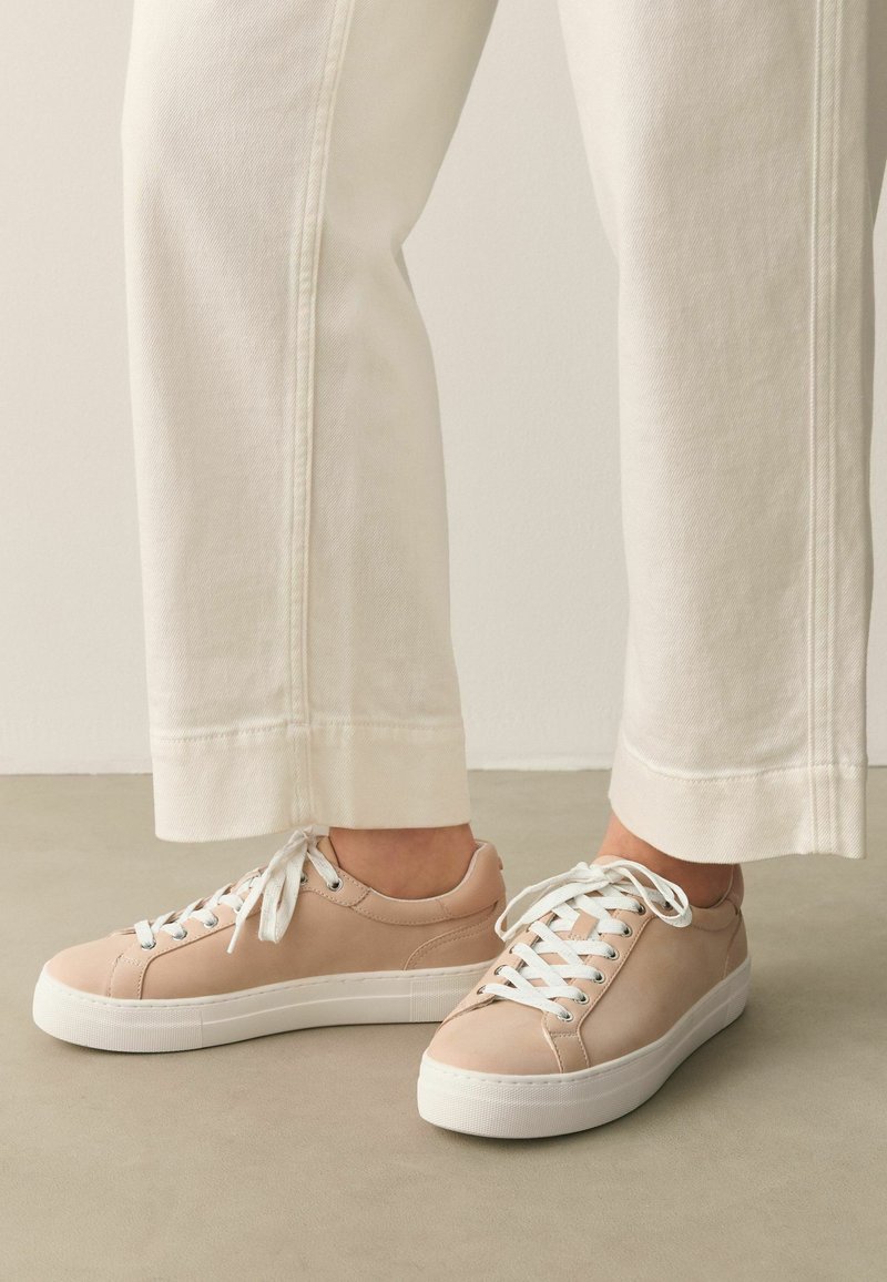 Baskets basses beige clair avec lacets blancs et semelles épaisses blanches portées avec un pantalon droit blanc cassé.