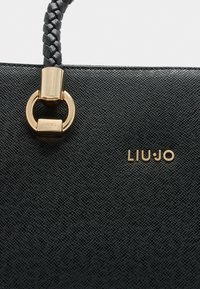 Sort tekstureret håndtaske med en flet-håndtag, gyldent hardware i cirkulær form, og mærkenavnet "LIU·JO" prægede i guld.