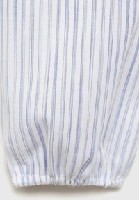 Primo piano di un tessuto con strisce verticali blu e bianche, caratterizzato da un orlo arricciato. La texture appare liscia e leggera.
