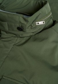 Olivgrüne Jacke aus weichem, glattem Stoff mit einem Reißverschlusskragen, Druckknopfakzenten und robusten Nähdetails.