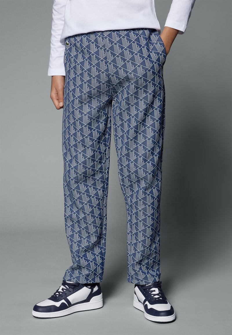 Pantalons bleus à motifs avec un design géométrique, taille élastique, poches latérales, associés à des baskets bleu marine et blanches.
