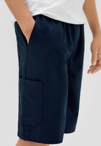 Marineblaue Shorts aus leichtem Stoff, mit einem elastischen Bund, seitlichen Taschen und einer einzelnen aufgesetzten Tasche am Oberschenkel.
