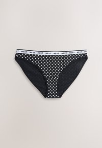Culottes de bikini à pois noirs avec une ceinture élastique blanche portant le nom de la marque "NEXT" répété. Tissu lisse, coupe taille basse.