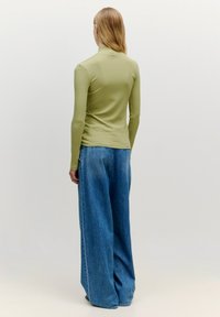 Hellgrünes, geripptes Rollkragenoberteil, kombiniert mit hochtaillierten, weit geschnittenen blauen Jeans. Strukturierter Stoff; lockere Passform.