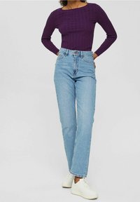 Lila gerippter Langarmshirt, kombiniert mit hoch taillierten hellblauen, gerade geschnittenen Jeans und weißen Sneakers; lässiges Outfit, das einfarbige Farben zur Schau stellt.